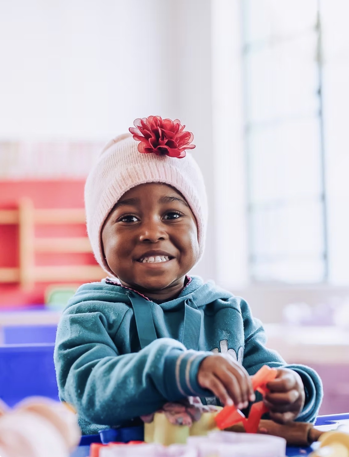 A smiling little girl playing with dough and cutters at a classroom table