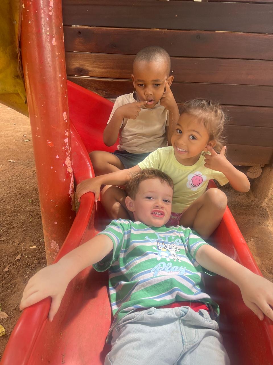 Three friends laughing together on the red playground slide