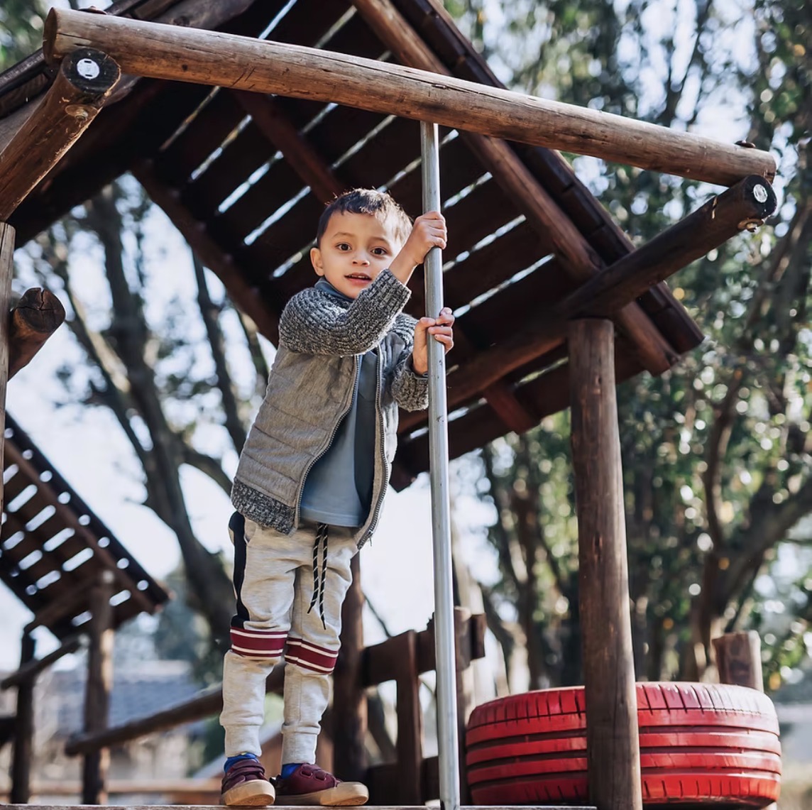 A little boy climbing the wooden jungle gym in the school garden